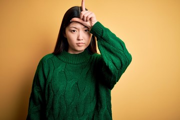 Young beautiful asian woman wearing green winter sweater over yellow isolated background making fun...
