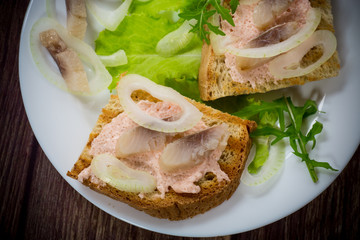 sandwich with salad, herring and herbs with onions in a plate