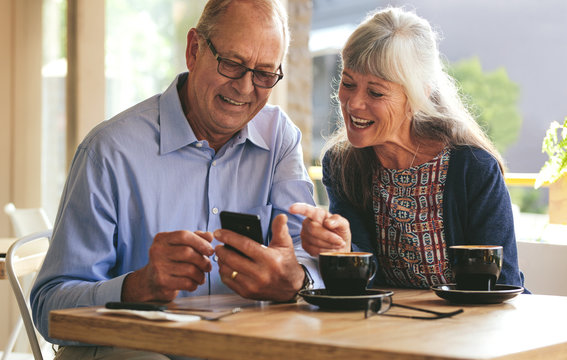 Senior couple using mobile phone at a cafe - Powered by Adobe