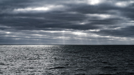 Mer grise dans l'orage et l'horizon lointain parsemé de faisceaux de lumière