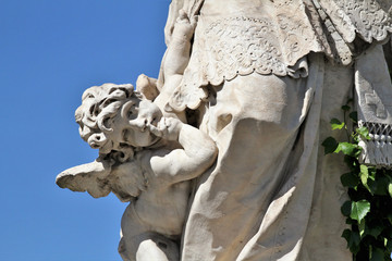 Detail of statue. Little angel in the foreground, blue sky in the background.