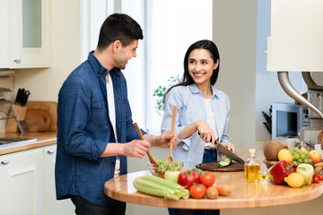 Cheerful couple preparing salad together at their home