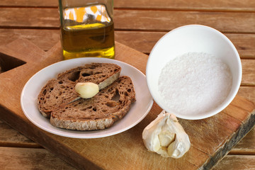 White ceramic plate with slices of bread and garlic clove, cup with salt and bottle of oil