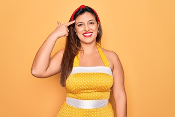 Young hispanic pin up woman wearing fashion sexy 50s style over yellow background Smiling pointing...