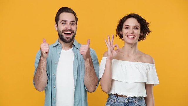 Young fun couple friends bearded guy girl 20s in casual clothes posing isolated on yellow background studio. People emotions lifestyle concept. Look at camera smiling say wow showing ok okay thumbs up