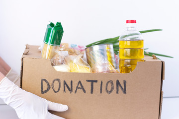 donation box. in hands in rubber gloves is a cardboard box with the inscription donation with food on a white background.