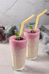 Two servings of homemade protein cocktail with frozen blackberries, banana and yogurt in glasses on gray concrete background, Diet and weight loss control concept