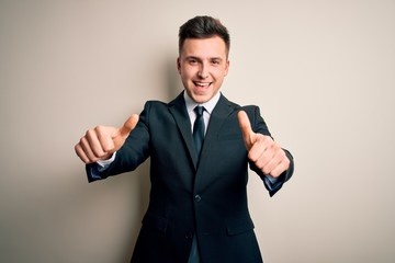 Young handsome business man wearing elegant suit and tie over isolated background approving doing positive gesture with hand, thumbs up smiling and happy for success. Winner gesture.