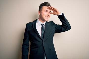 Young handsome business man wearing elegant suit and tie over isolated background very happy and smiling looking far away with hand over head. Searching concept.