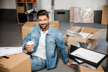 Merry handsome man celebrating housewarming with cup of coffee