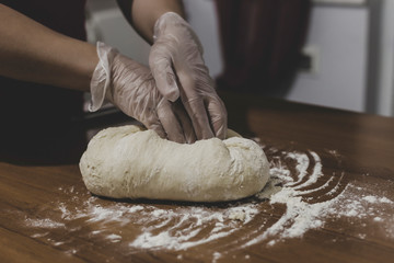 Hands of a woman making dough with plastic gloves on the table