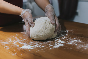 Hands of a woman making dough with plastic gloves on the table