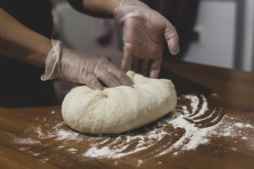 Hands of a woman making dough with plastic gloves on the table