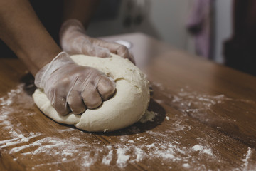 Hands of a woman making dough with plastic gloves on the table