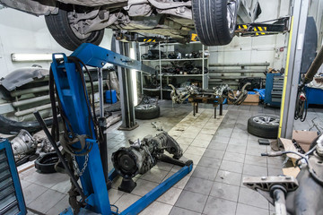 A raised car on a blue crane for engine or gearbox repair in a car workshop against the background of removed spare parts - wheels, rear axle axis.