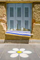 Part of modern building. Window with closed shutters. Architecture. Exterior, fragment. Flower painted on tiled floor outdoor. Place to sit down on windowsill outdoor. Window with old louvers