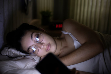 woman lying in bed with insomnia looking at cell phone