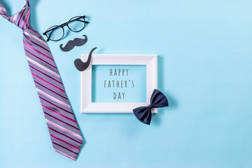 Happy fathers day concept. Top view of tie, glasses, mustache, white picture frame with LOVE DAD text on bright blue pastel background. Flat lay.