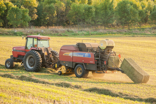 Close-up of baling hay with a Case IH 7130 tractor and New Holland BB9060 baler on a summer evening with a big bale coming out of the baler.