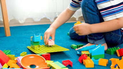 Closeup image of little boy sitting on floor and playing with toy blocks