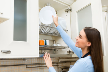 Young girl putting or taking clean plate on shelf