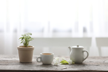 White tea cup and tea pot with plant on wooden table minimal interior  