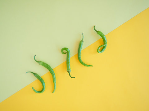 five isolated green chili peppers on a simetrical vibran yelow surface