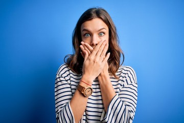 Young beautiful blonde girl wearing casual sweater standing over blue isolated background shocked covering mouth with hands for mistake. Secret concept.