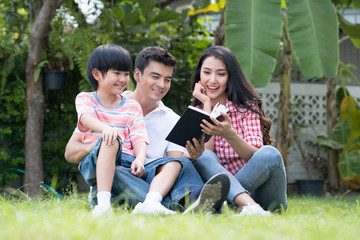Father and mother sit in the garden at home, They are teaching a lovely son to read a book, Happy...