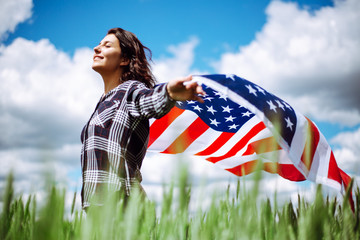Young woman waves an american flag on the green wheat field. Patriotic holiday celebration. United States of America independence day, 4th of July concept.