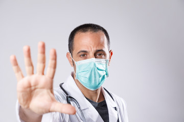 medico con camice bianco e mascherina chirurgica fa il segno di stop con la mano aperta, isolato su sfondo bianco
