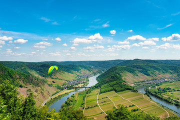 Man flying a green paraglider over beautiful wineries in Germany, visible river and forest.