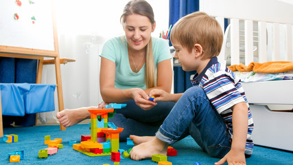 Portrait of happy smiling boy with young mother playing on floor with colorful toys