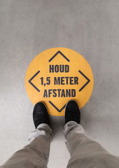 A person standing on a social distancing sign. Translation of Dutch text: “Keep 1.5 meter distance”. - 352596685