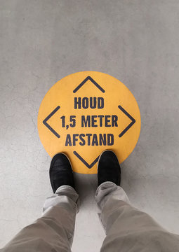 A person standing on a social distancing sign. Translation of Dutch text: “Keep 1.5 meter distance”.