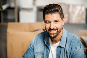 Joyful bearded man near carton boxes in empty apartment