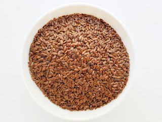 Flax seeds in a white ceramic plate on a white background.