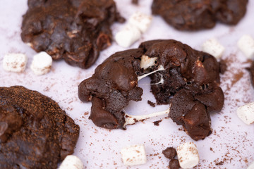 Close up of baked dark chocolate cookies with marshmallow that divided, with their ingredients on white background.
