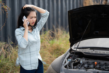 A beautiful Asian woman uses a smartphone to contact a broken car mechanic 