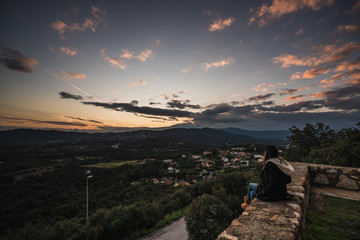 mujer mirando de espaldas desde un castillo al atardecer en los campos españoles con un cielo...