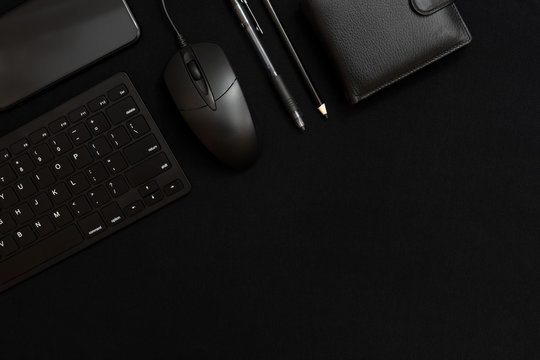 Black smartphone, keyboard, pencil, pen, wallet and black computer mouse on a black background. Business items. Low key photo. Free space for text. Dark on dark.