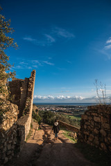 mujer mirando de espaldas al valle desde la cima de una montaña donde hay un castillo destruido