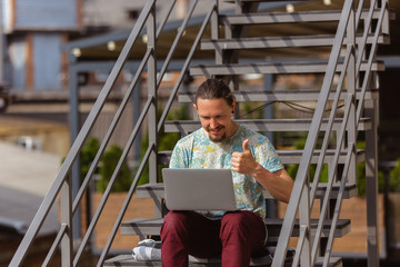 Obraz premium Thumb up. Young man, businessman working outdoors concentrated, looking on laptop screen, monitor. Copyspace for your ad. Finance, business, work, gadgets and tech concept. Freelance, remote worker.