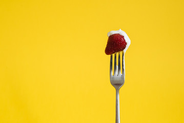 Macro shot of ripe strawberries on a fork with sour cream. Closeup red berry with yellow background - 352600244