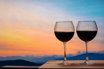 Glasses of red wine against sunset, red wine on the sky background with clouds