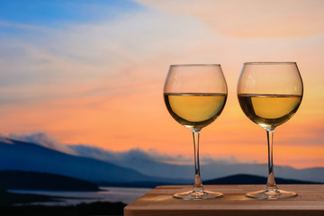 Romantic glass of wine sitting on the beach at colorful sunset. Glasses of white wine against sunset, white wine on the sky background with clouds - 352600289