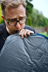 Close up of man with glasses blowing up a self inflatable sleeping pad for camping  