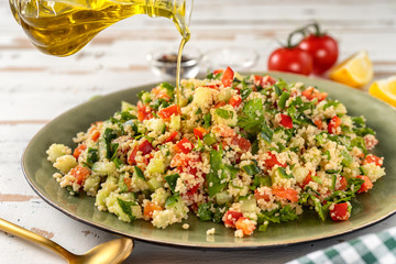 Pouring an olive oil into a big plate with vegan fresh couscous salad