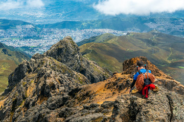 Fototapeta premium A mountain climber with ropes and walking sticks enjoying the view and making a phone call after reaching the Rucu Pichincha Volcano Peak, Quito, Ecuador.