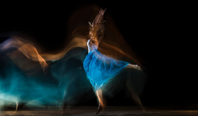 Fototapeta na wymiar larga exposición de una bailarina con vestido blanco y azul y fondo negro con mucho movimiento